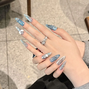 Blue almond press-on nails with 3D white swan, pearls, and chains on a grey background