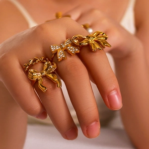 Golden bow ring set with white cubic zirconia and pearls on polished stainless steel