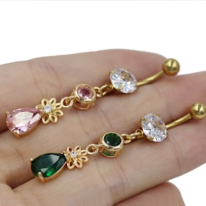 Gros plan de piercings de nombril dorés avec zircons roses et verts tenus par la main