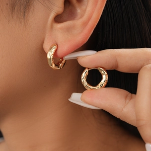 Detail of gold textured round geometric hoop earrings worn by a model in a close-up view