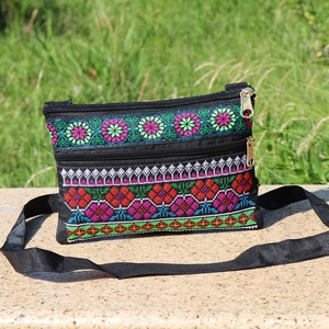 Detail of black crossbody bag with colorful ethnic embroidery and double zippers