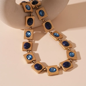 Close-up of vintage gold necklace with blue resin square links on a white art stand