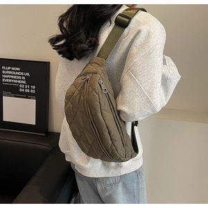 Detail of army green quilted crossbody bag with wide strap and silver zipper on model