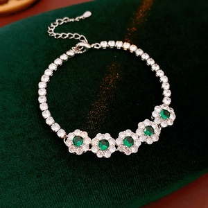 Détail d'un bracelet fleur en argent avec pierres vertes sur un fond en velours vert