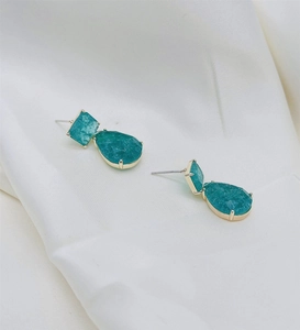 Detail of teal matte irregular stones set in gold geometric drop earrings on silk