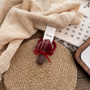 Detail of fabric mushroom hair tie with brown plaid pattern and red bow on woven mat