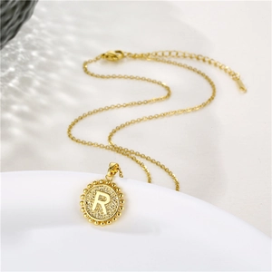 Close-up of gold round pendant with letter R and beaded edge on stainless steel chain