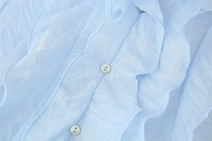 Close-up of light blue chiffon fabric with ruffled layers and shell-like buttons
