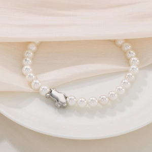 Detail of shell pearl bracelet with cute silver pig pendant on elegant beige silk fabric