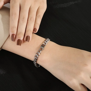 Silver Cuban link bracelet worn by a model against a dark fabric background close-up