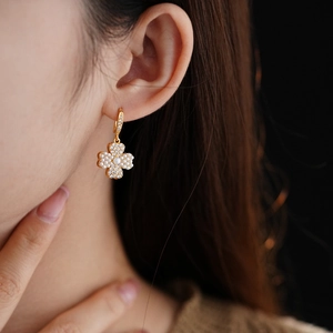 Close-up of gold-plated clover earrings with white pearls and sparkling zircons