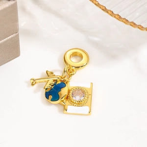 Detail of gold charms featuring plane, map, and camera with blue enamel and zircon inlay