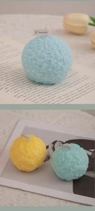 Detailed view of spherical embossed rose and leaf patterned scented candles in pastel colors