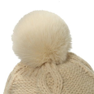 Detailaufnahme einer beigen Strickmütze mit flauschigem Kunstfell-Bommel und Zopfmuster