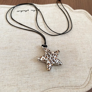 Detail of star-shaped leopard print pendant necklace on natural linen background
