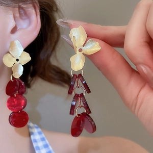 Macro view of long tiered earrings with golden flower studs and red acrylic sequins
