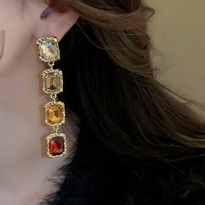 Close-up of long gold earrings featuring four cascading colorful square gemstones on a model