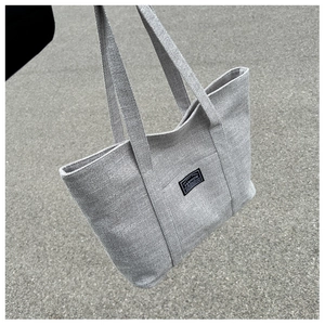 Close-up of grey canvas tote bag with fashion label and textured fabric details