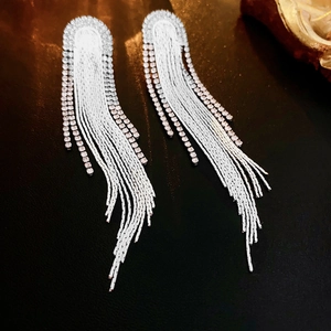 Macro shot of silver tassel earrings with crystals on a textured black leather background
