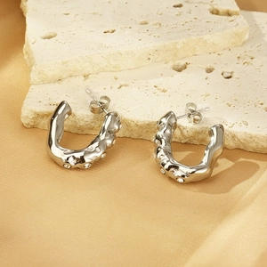 Close-up of silver U-shaped earrings with rhinestones on stone and satin background
