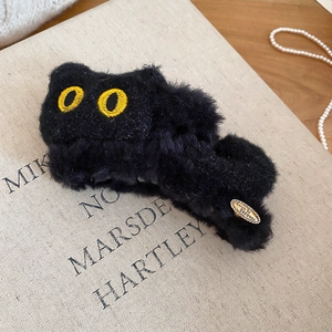 Détail d'une pince à cheveux chat en peluche noire sur un livre en tissu beige vintage