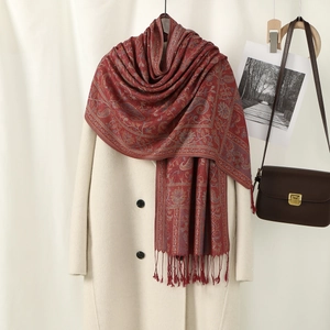 Red paisley jacquard scarf with tassels on display with beige coat for women