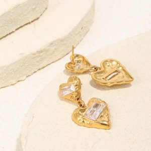 Detail of 18K gold plated heart earrings with zircon inlay on a textured stone background