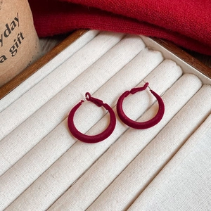Detail shot of deep red velvet hoop earrings displayed on a beige jewelry tray