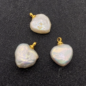 Macro shot of three white heart-shaped baroque pearl pendants with gold rings on black background