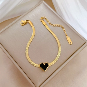 Macro detail of gold snake chain bracelet with black heart pendant on silk background