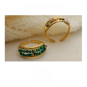 Close-up of gold titanium steel rings with malachite and tourmaline beads on knit fabric