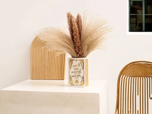 Macro shot of book-shaped ceramic vase with gold text and dried reed flowers