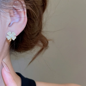 Close-up of a model wearing sparkling gold clover stud earrings with pavé zircon stones