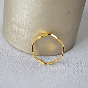 Detail of minimalist wavy gold-plated brass ring on a textured grey fabric background
