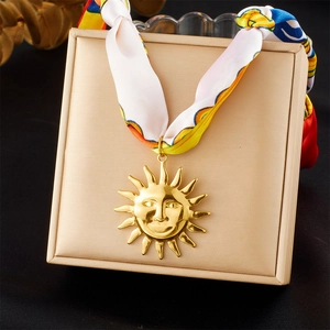 Détail d'un collier pendentif soleil doré avec ruban de soie coloré dans un coffret à bijoux
