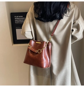Detail of vintage brown bucket bag with gold chain on model wearing beige trench coat