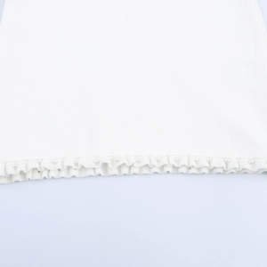 Detailed view of the white knit dress hem featuring ruffle edges and pearl embellishments