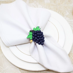 Macro detail of a blue grape napkin ring with green leaves on a white linen napkin