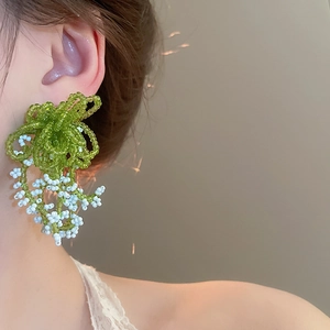 Close-up of handmade green and white floral beaded tassel earrings on model ear