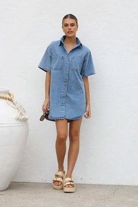 Detail of short sleeve denim shirt dress with front buttons and chest pockets in blue