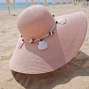 Detail of pink straw sun hat featuring seashell and wooden bead decorative band