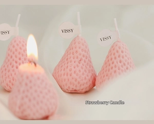 Macro shot of realistic strawberry-shaped candles with textured surface and burning wick