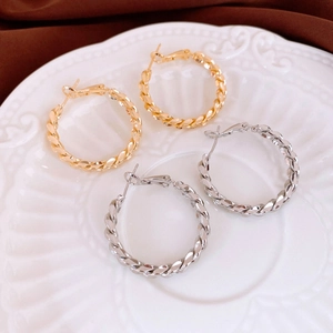 Minimalist twisted metal hoop earrings in gold and silver finish on white relief plate