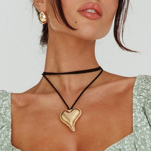 Close-up of golden heart pendant on black cord and matching teardrop earrings set