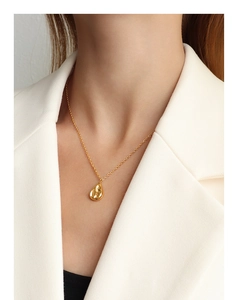 Macro detail of gold irregular water-drop pendant necklace on a model's neck