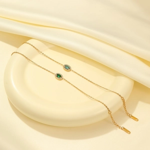 Elegant gold chain necklace with emerald and blue zircon oval pendants on silk background
