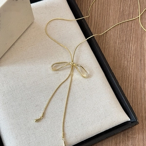 Close-up of golden bow-shaped pendant on a delicate snake chain necklace display