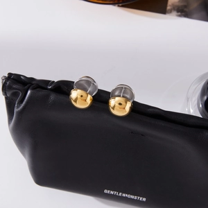 Close-up of polished gold hemispherical stud earrings on a textured black leather pouch