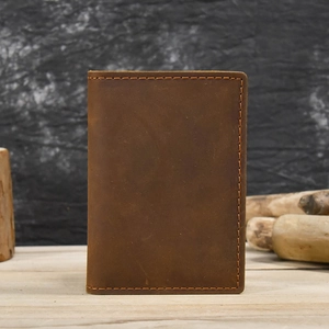 Vertical view of a vintage dark brown leather passport holder on a rustic wooden desk