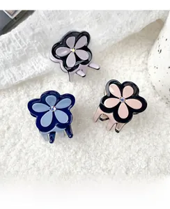 Vue détaillée de trois pinces à cheveux fleur en acétate violet, bleu et rose sur peluche